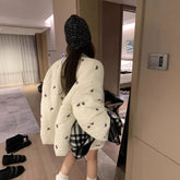 Person wearing a white quilted jacket with black bee patterns in a room.